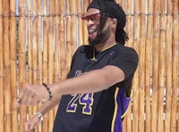 a man with dreadlocks in front of a bamboo fence