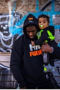 a man holding a child in front of a graffiti covered wall